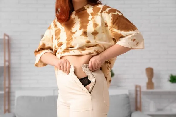 Image of woman trying to do her trousers up after pregnancy weight gain Kingswinford